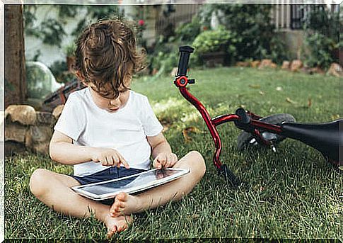 Child sitting on home garden lawn using tablet.