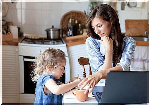 Mother having coffee in the kitchen and watching her daughter make a drawing.